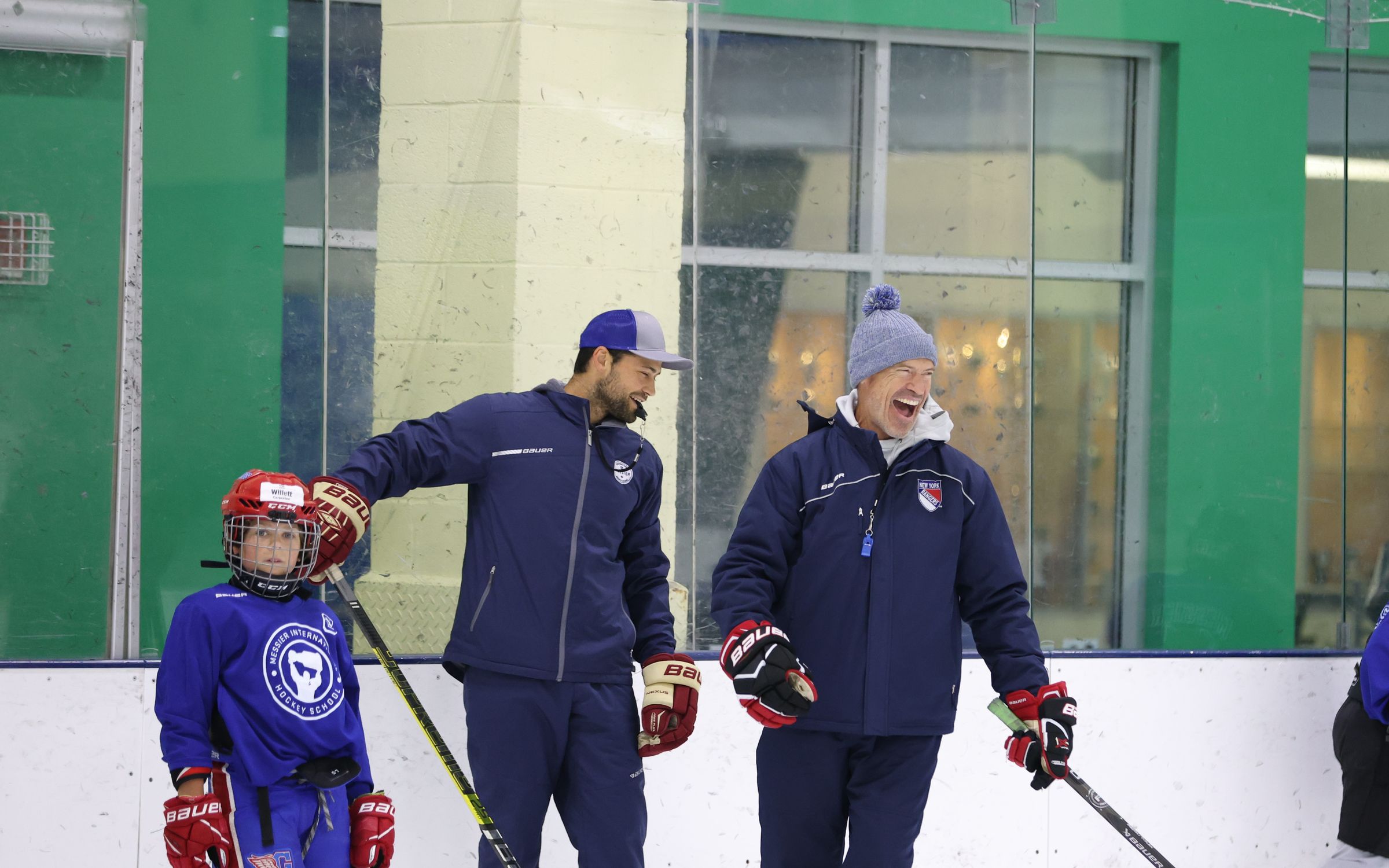 Mark Messier laughing with a coach at the boards during a hockey school session